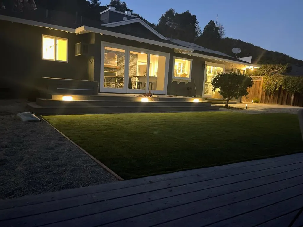 Backyard deck and lawn with landscape lighting at dusk