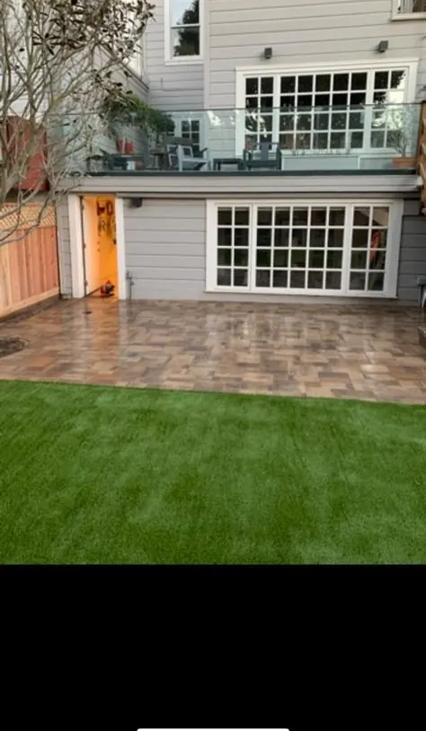Backyard paver patio under a deck with artificial turf beyond