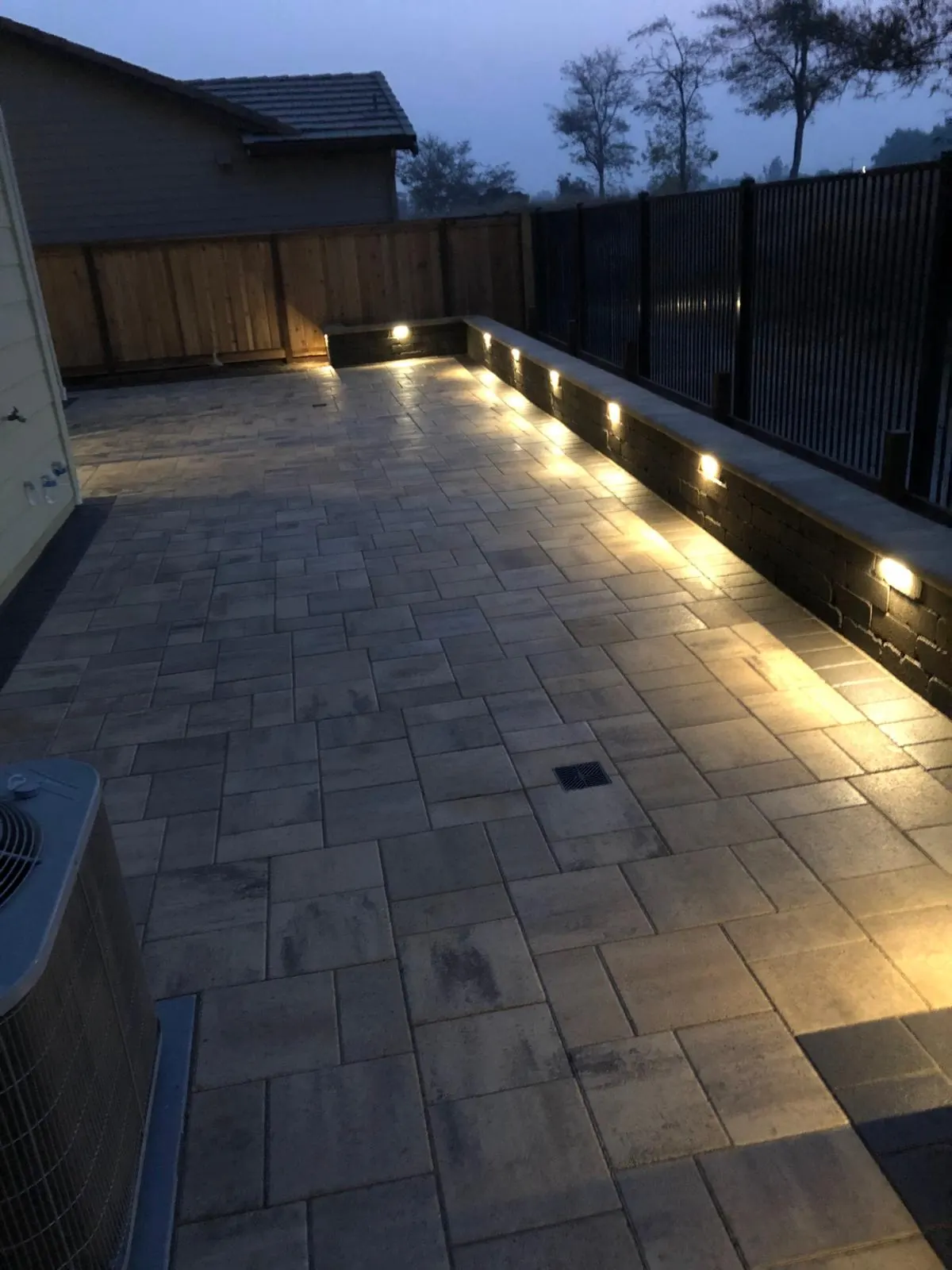 Paver patio with a low retaining wall and built-in step lights at dusk