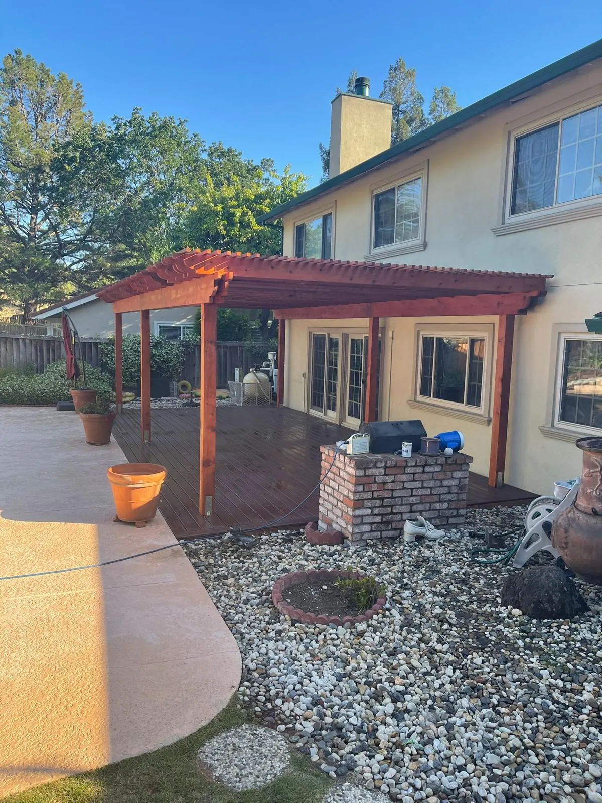 Wood pergola over a concrete patio with a rock garden